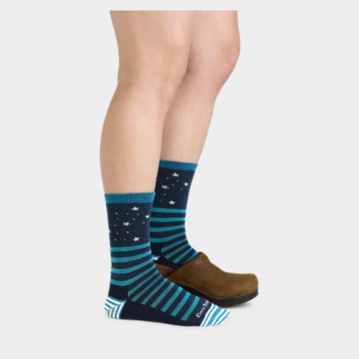 Darn Tough 6037 Animal Haus Lightweight Cushion Crew women&#39;s sock featuring navy blue sock with teal stripes and stars at top. Sock shown on model wearing one shoe. 