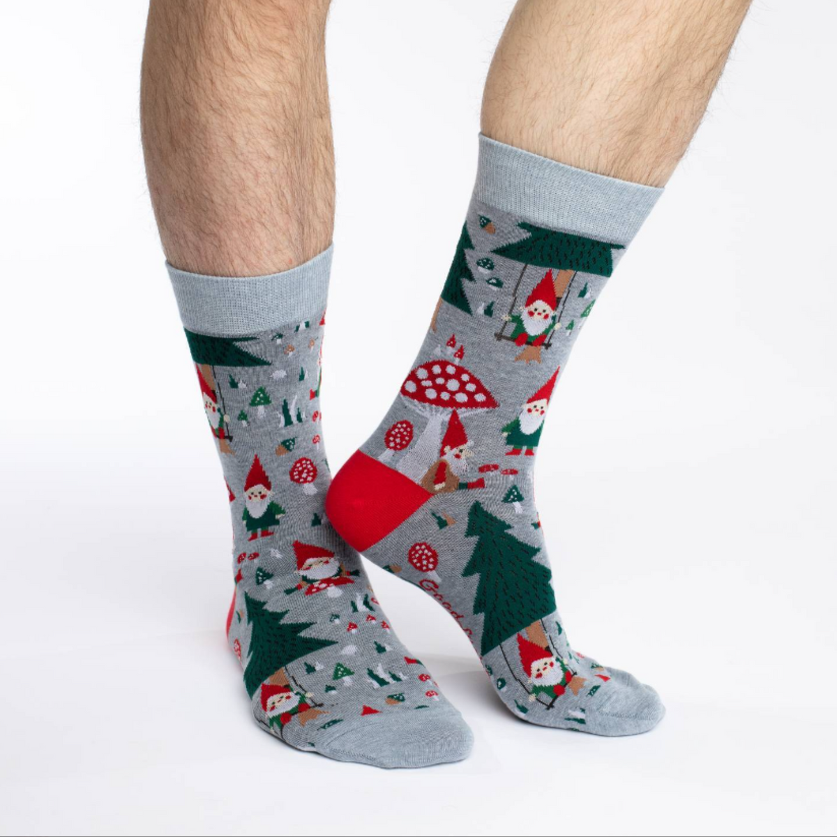 Good Luck Sock Woodland Gnomes women&#39;s and men&#39;s crew socks featuring gray sock with gnomes in red hats, mushrooms, and trees all over. Socks worn by male model. 