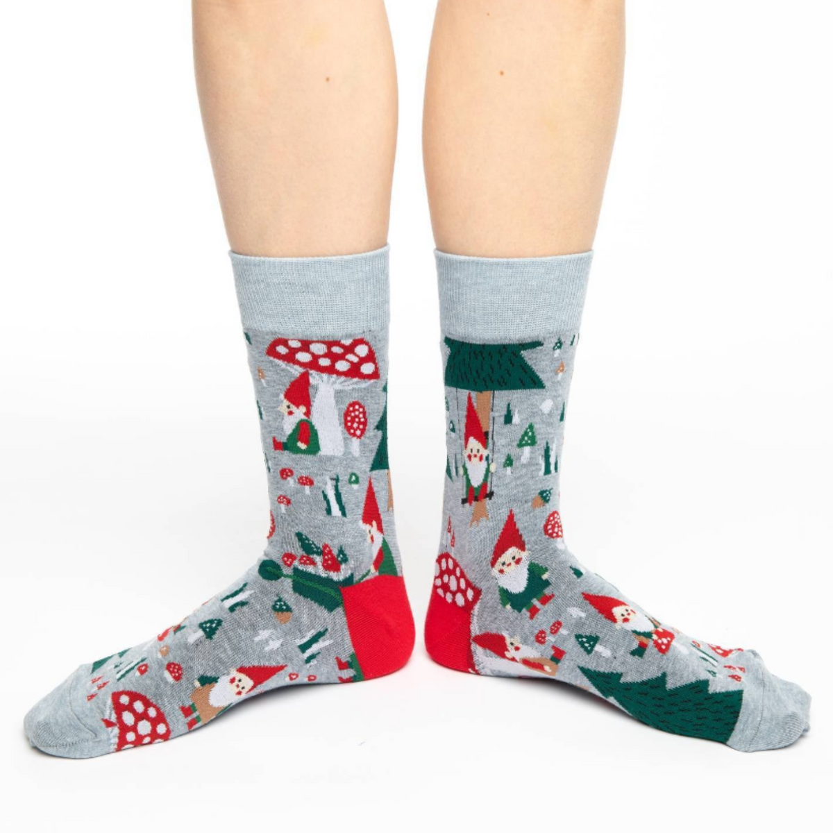 Good Luck Sock Woodland Gnomes women&#39;s and men&#39;s crew socks featuring gray sock with gnomes in red hats, mushrooms, and trees all over. Socks worn by female model. 