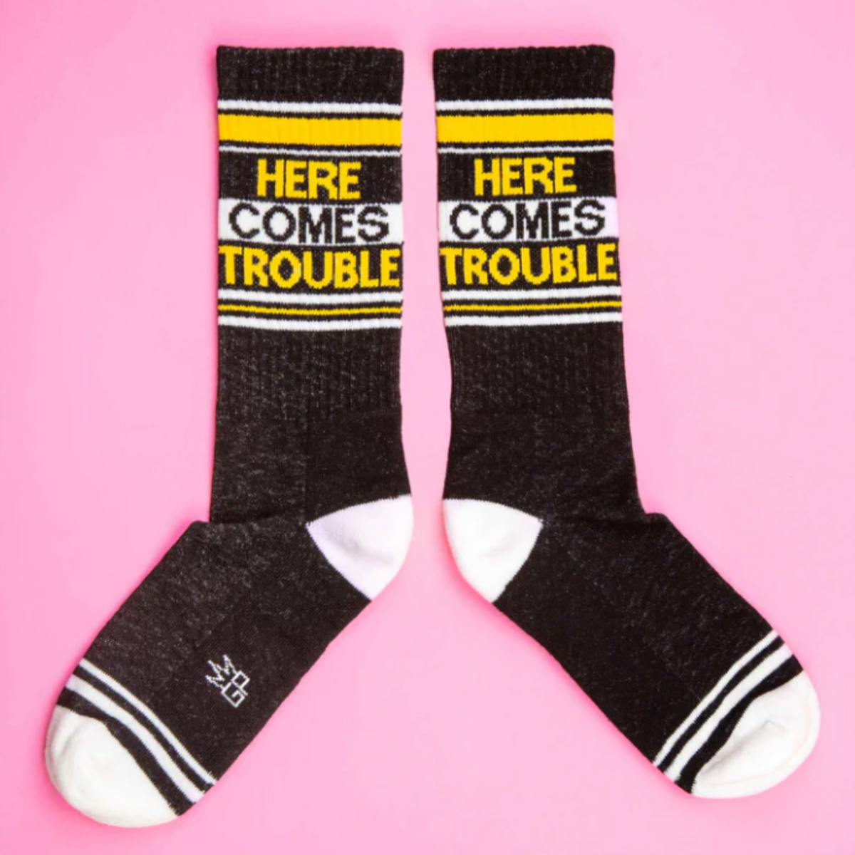 Gumball Poodle Here Comes Trouble women&#39;s and men&#39;s sock featuring black sock with white and yellow &quot;here comes trouble&quot; in capital letters on display 