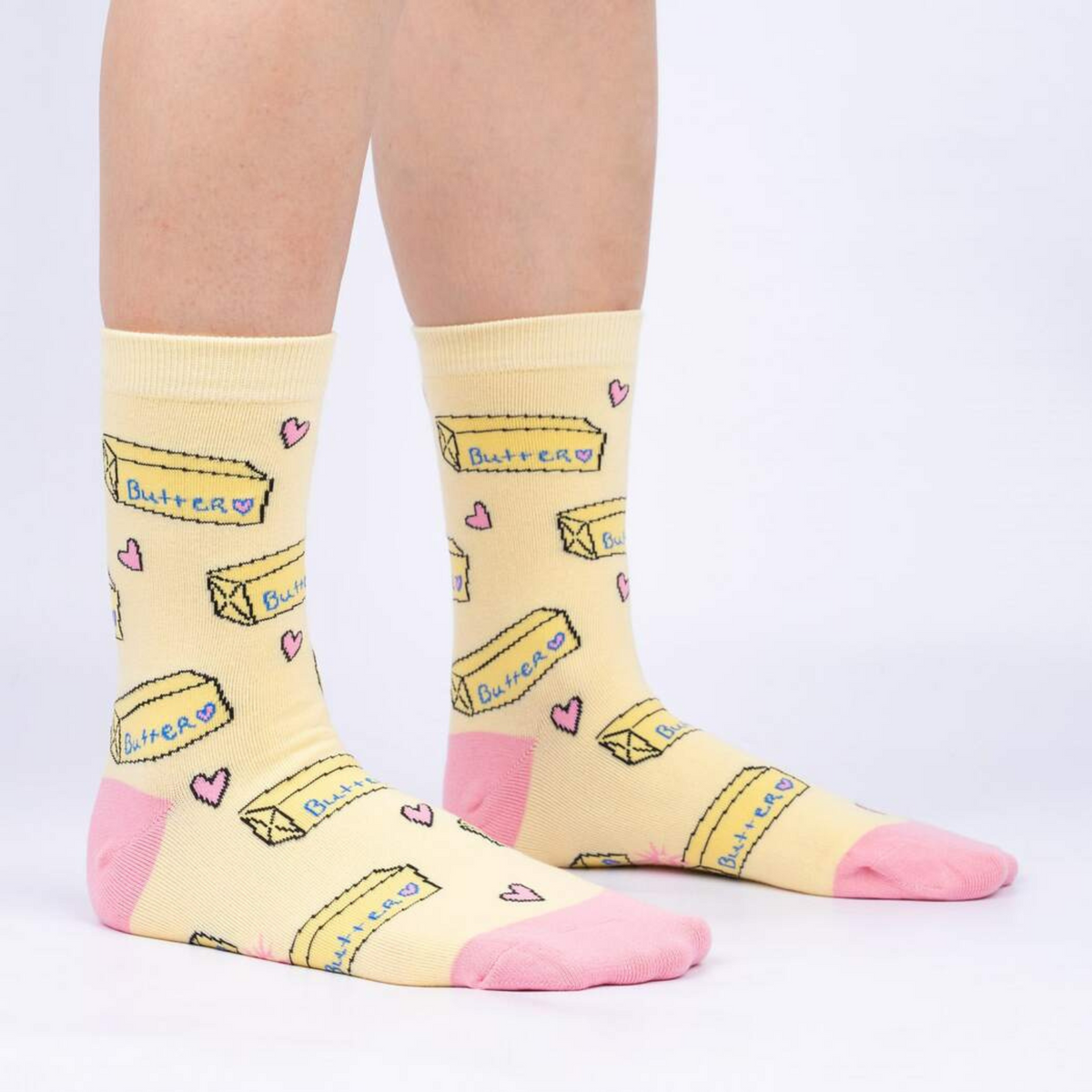 Sock It To Me Butter Me Up women&#39;s yellow crew sock featuring pink hearts, heel and toe with sticks of butter all over on model from side
