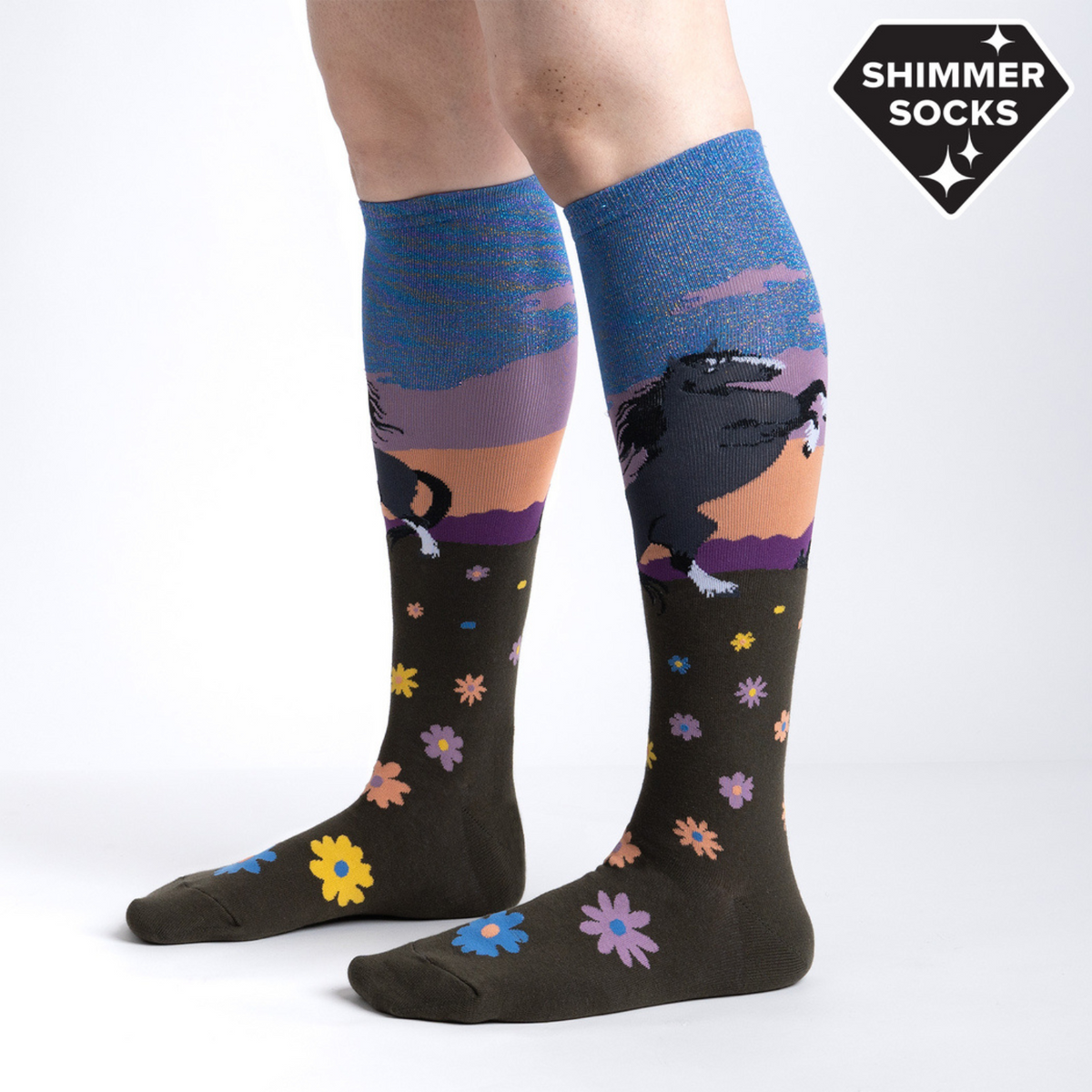 Sock It To Me Black Beauty women&#39;s knee high sock featuring shimmery blue sky with black horse rearing on it&#39;s back legs over a field of flowers worn by model seen from side