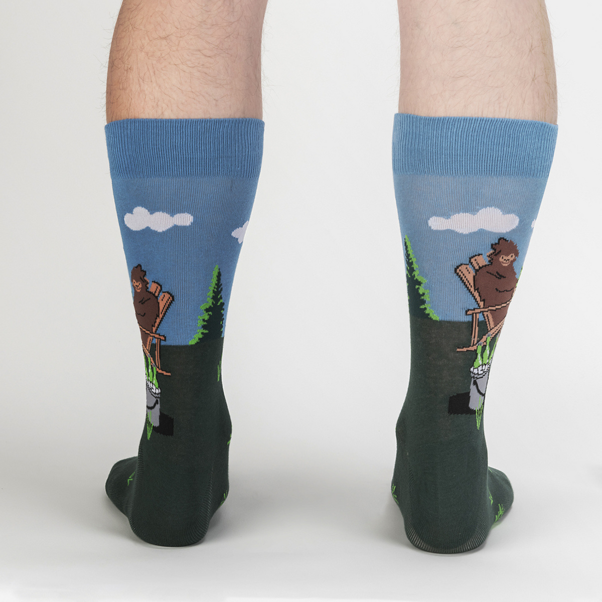 Sock It To Me Bucket List men&#39;s crew sock featuring Sasquatch sitting on a lawn in a chair drinking beer with a bucket of beer shown on model from back