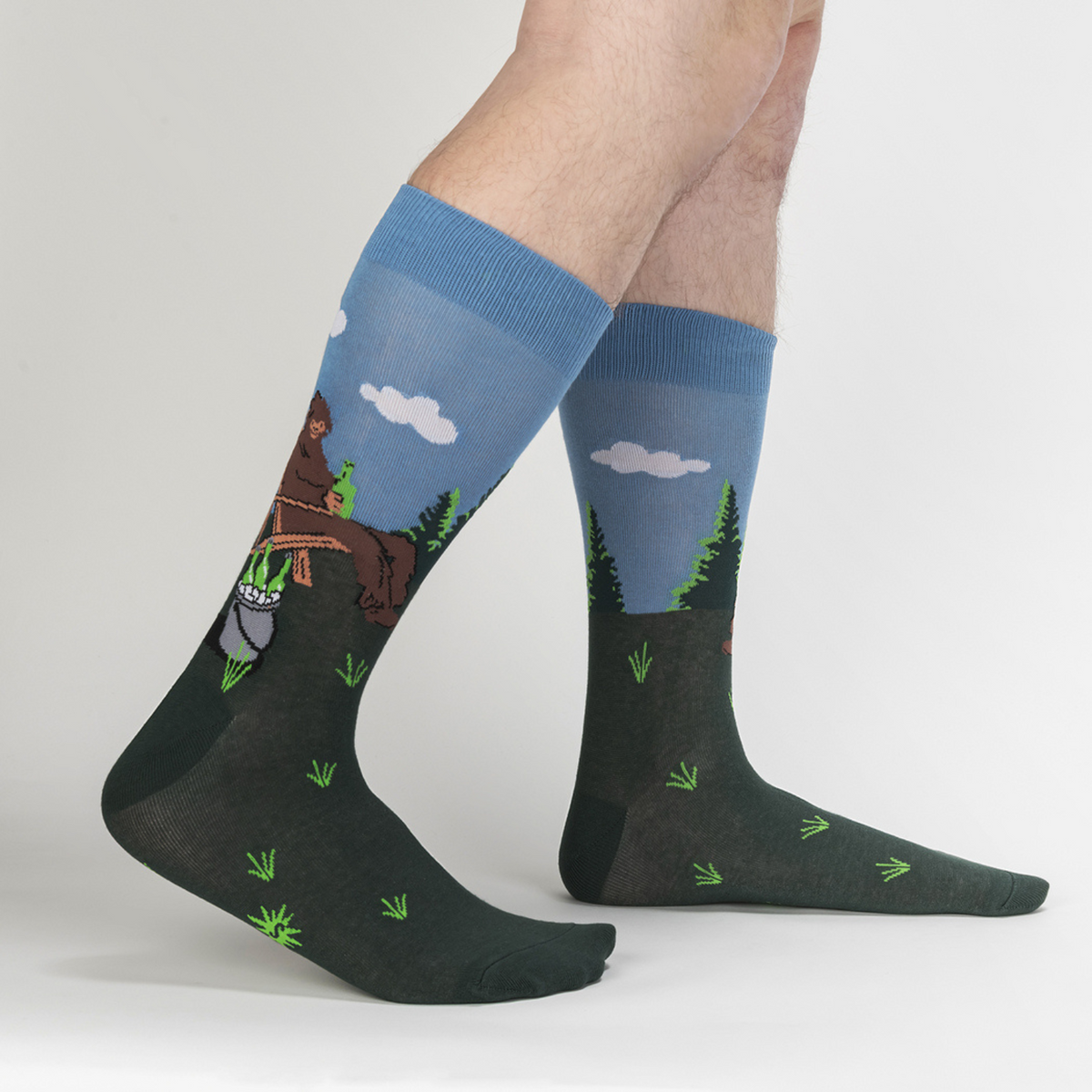 Sock It To Me Bucket List men&#39;s crew sock featuring Sasquatch sitting on a lawn in a chair drinking beer with a bucket of beer shown on model from side
