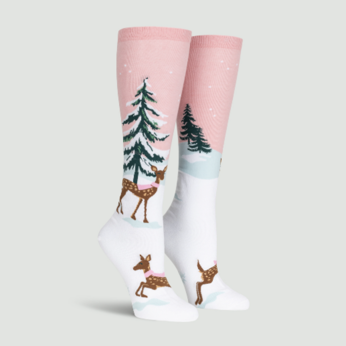 Sock It To Me Doe-nt Forget Your Scarf women&#39;s knee high sock featuring pink sock with snow-covered fir tree and deer with pink scarf. Socks shown on display feet seen from side. 