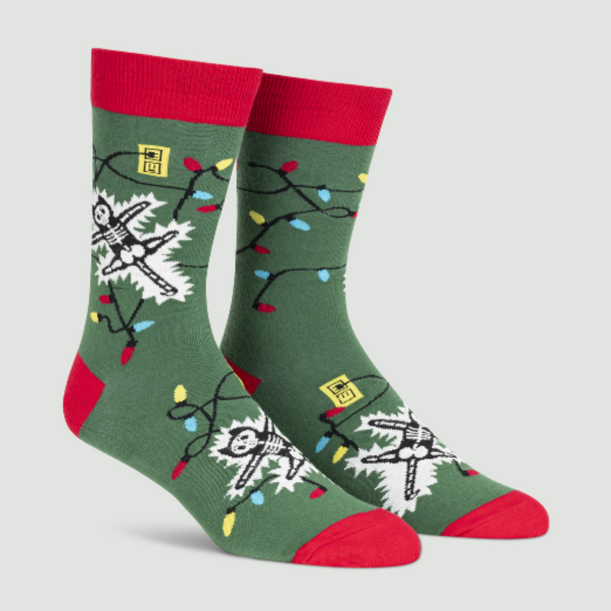 Sock It To Me Eating Light This Holiday (GLOWS IN THE DARK) women&#39;s and men&#39;s crew socks featuring green sock with red cuff, heel, and toe with cartoon cat being electrocuted by Christmas lights. Socks shown on display feet. 