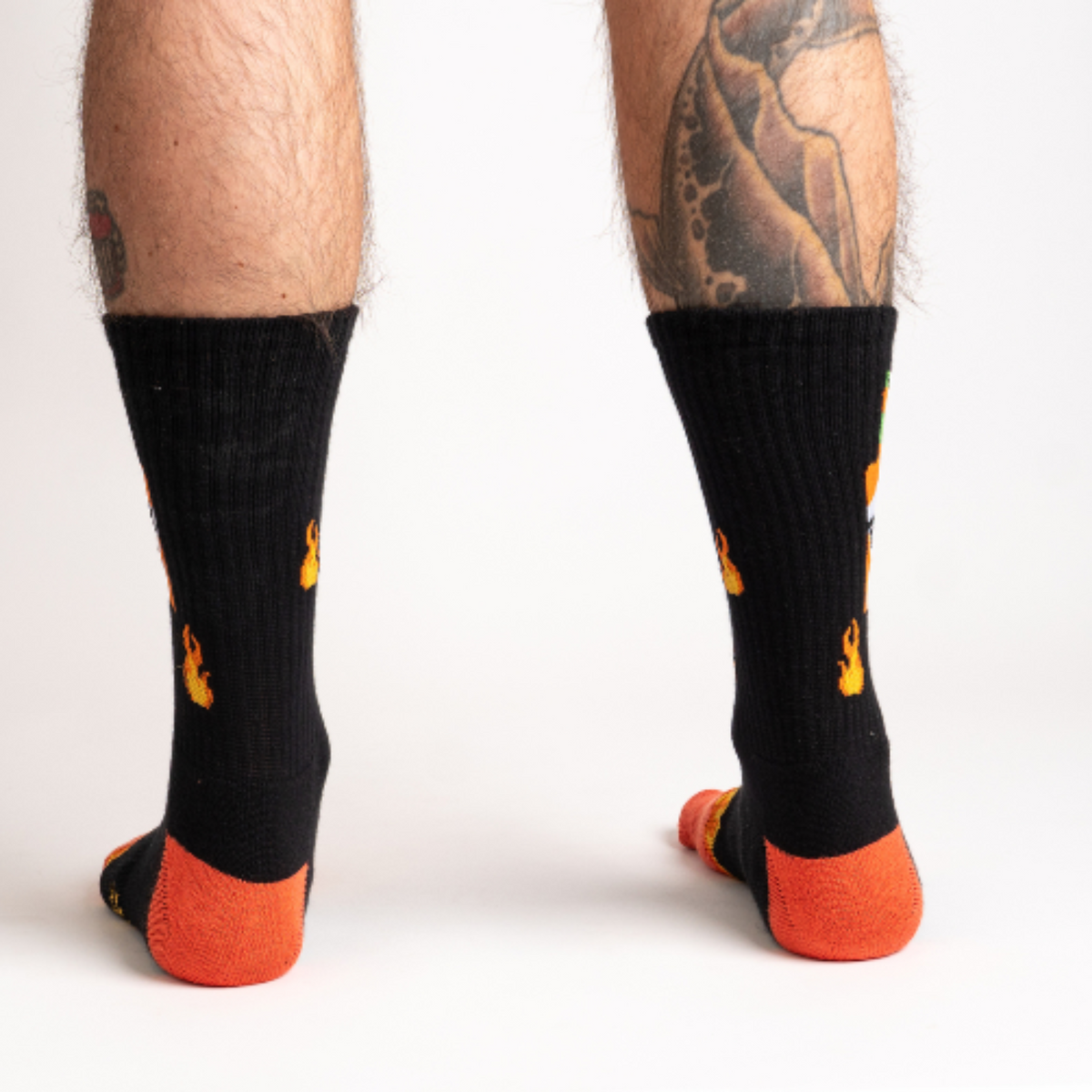 Sock It To Me Fire athletic crew men&#39;s sock featuring black socks with an image of flames and hot sauce bottle. Socks shown on model from behind.. 