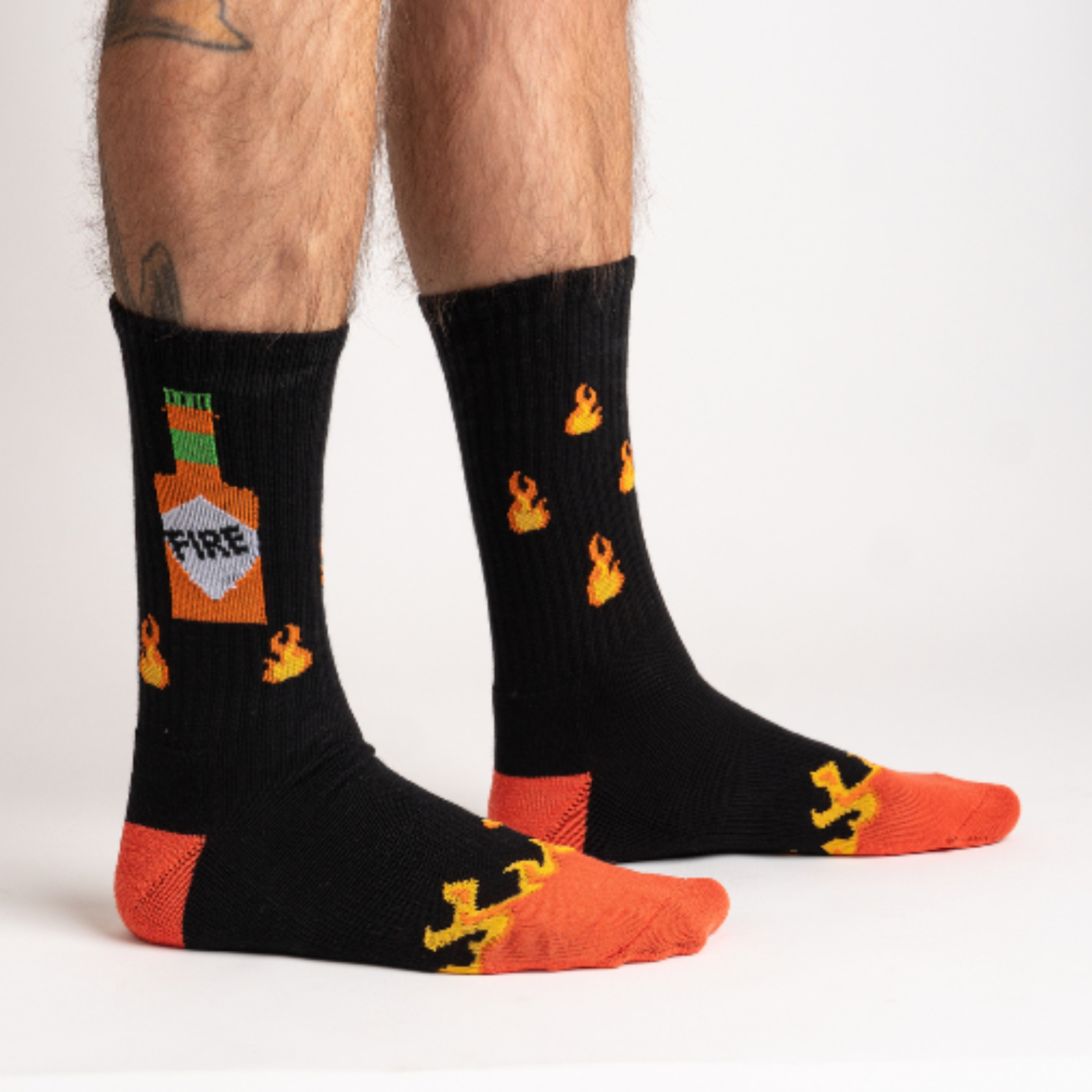 Sock It To Me Fire athletic crew men's sock featuring black socks with an image of flames and hot sauce bottle. Socks shown on model from side. 