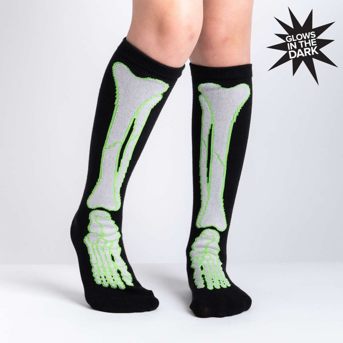 Sock It To Me It&#39;s Going Tibia Good Day kids&#39; sock (GLOW IN THE DARK!) featuring a black knee high sock with outline of tibia bones worn by model from front