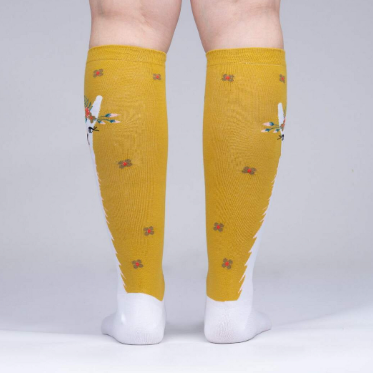 Sock It To Me Llama Queen women&#39;s sock featuring goldenrod knee high sock with white llama wearing a floral crown worn by model seen from behind. .