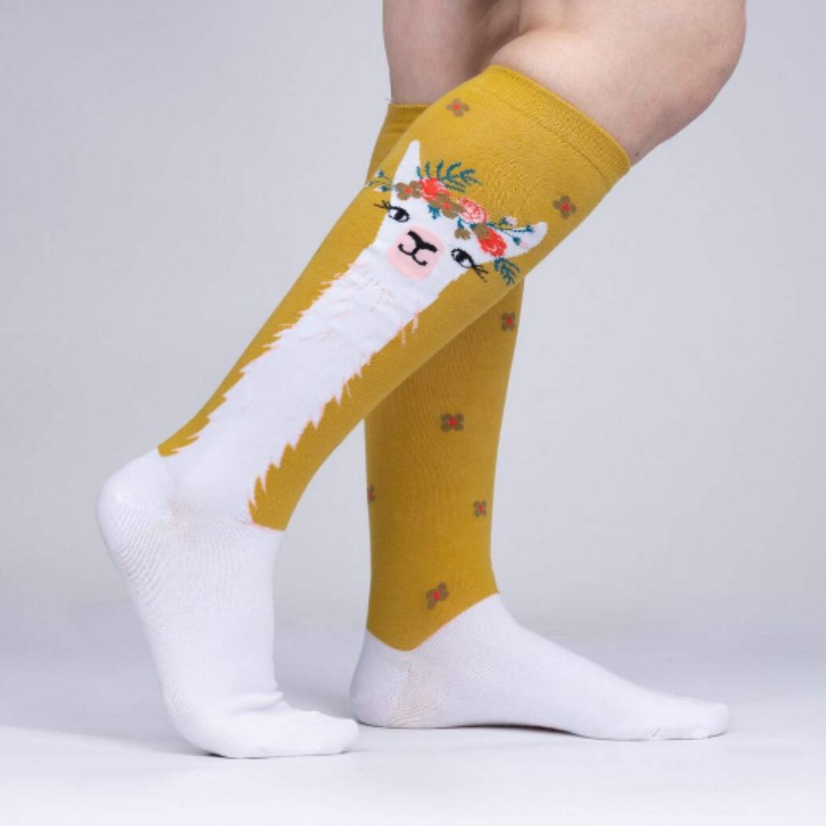 Sock It To Me Llama Queen women&#39;s sock featuring goldenrod knee high sock with white llama wearing a floral crown worn by model seen from side.