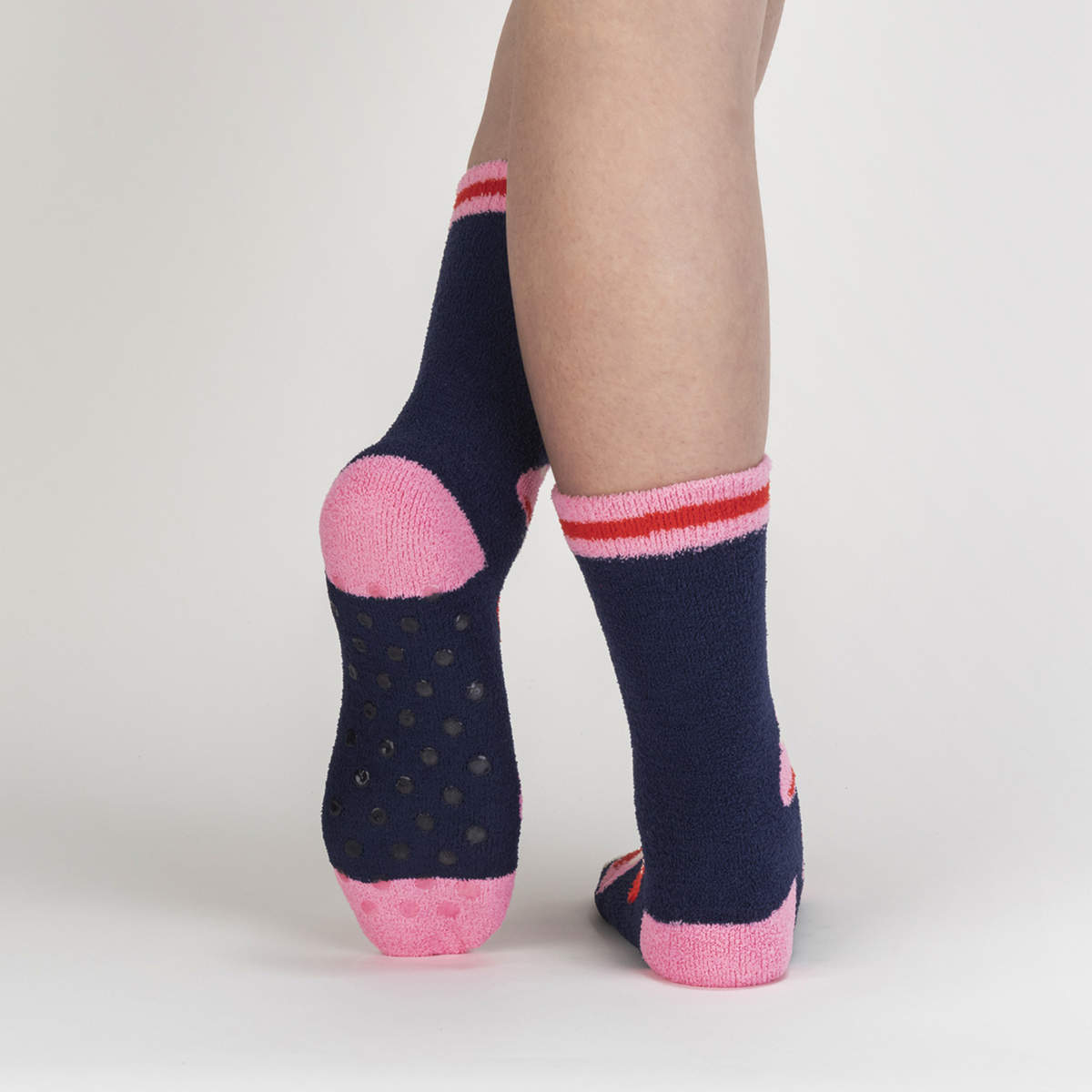 Sock It To Me Magic Mushrooms women&#39;s slipper sock featuring smiling red cap mushrooms on blue slipper sock with grips on bottom worn by model from back showing grippers on bottom of slipper