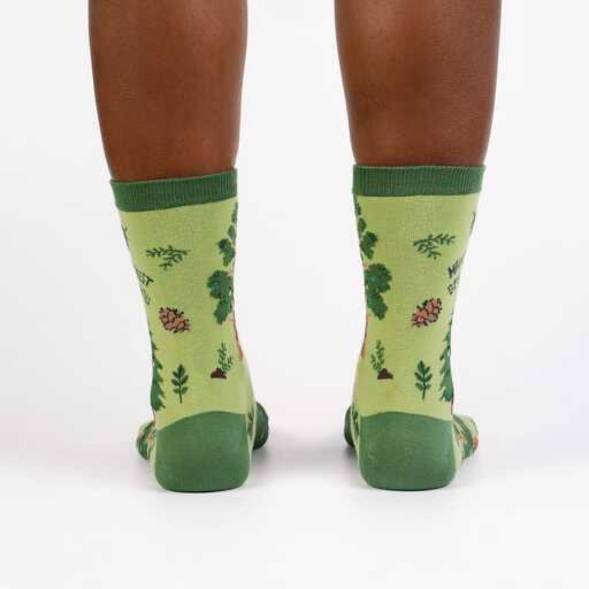 Sock It To Me May the Forest Be With You women&#39;s crew sock featuring a green sock with trees and pinecones and &quot;May the forest be with you&quot; written. Socks worn by model seen from behind. 