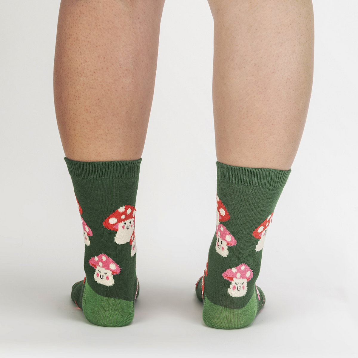 Sock It To Me Mellow Mushrooms women&#39;s sock featuring a green crew sock with red capped smiling mushrooms all over worn by a model from back