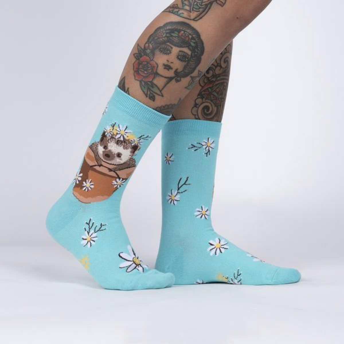 Sock It To Me My Dear Hedgehog women&#39;s crew sock featuring light blue sock with flowers all over and a hedgehog in a flower pot. Socks worn by model seen from side. 