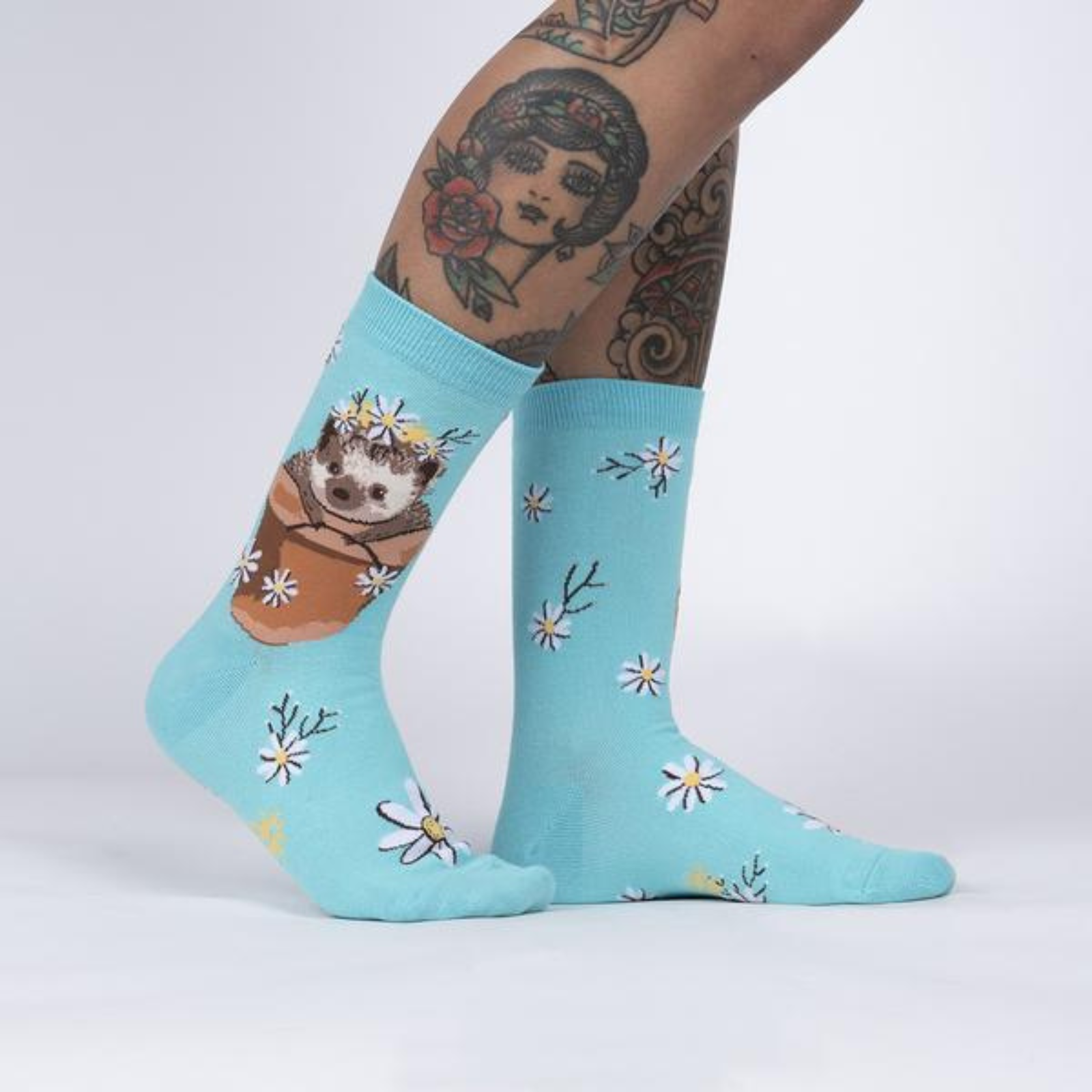 Sock It To Me My Dear Hedgehog women's crew sock featuring light blue sock with flowers all over and a hedgehog in a flower pot. Socks worn by model seen from side. 