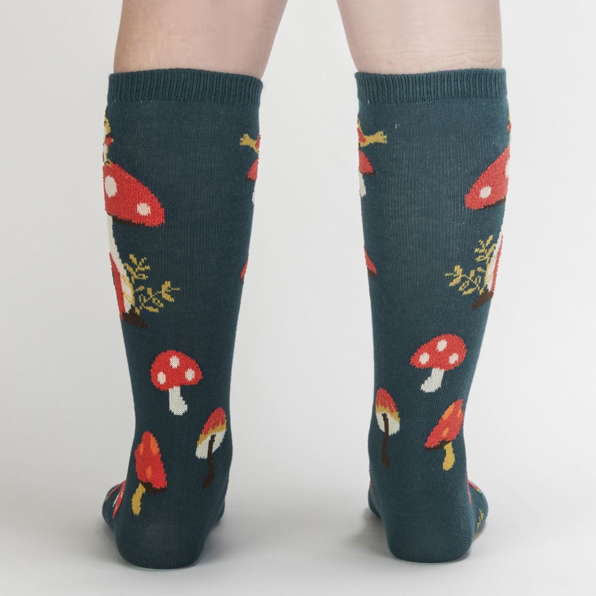 Kids&#39; Sock It To Me Shroom and Board women&#39;s and kids&#39; sock featuring green knee high with deer, squirrel, and mushrooms all over worn by model seen from behind