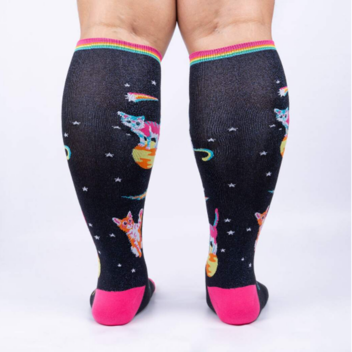 Sock It To Me Space Cats extra-stretchy knee sock featuring pink toe and heel with shimmery black background and kittens in outer space. Socks worn by model seen from back.. 