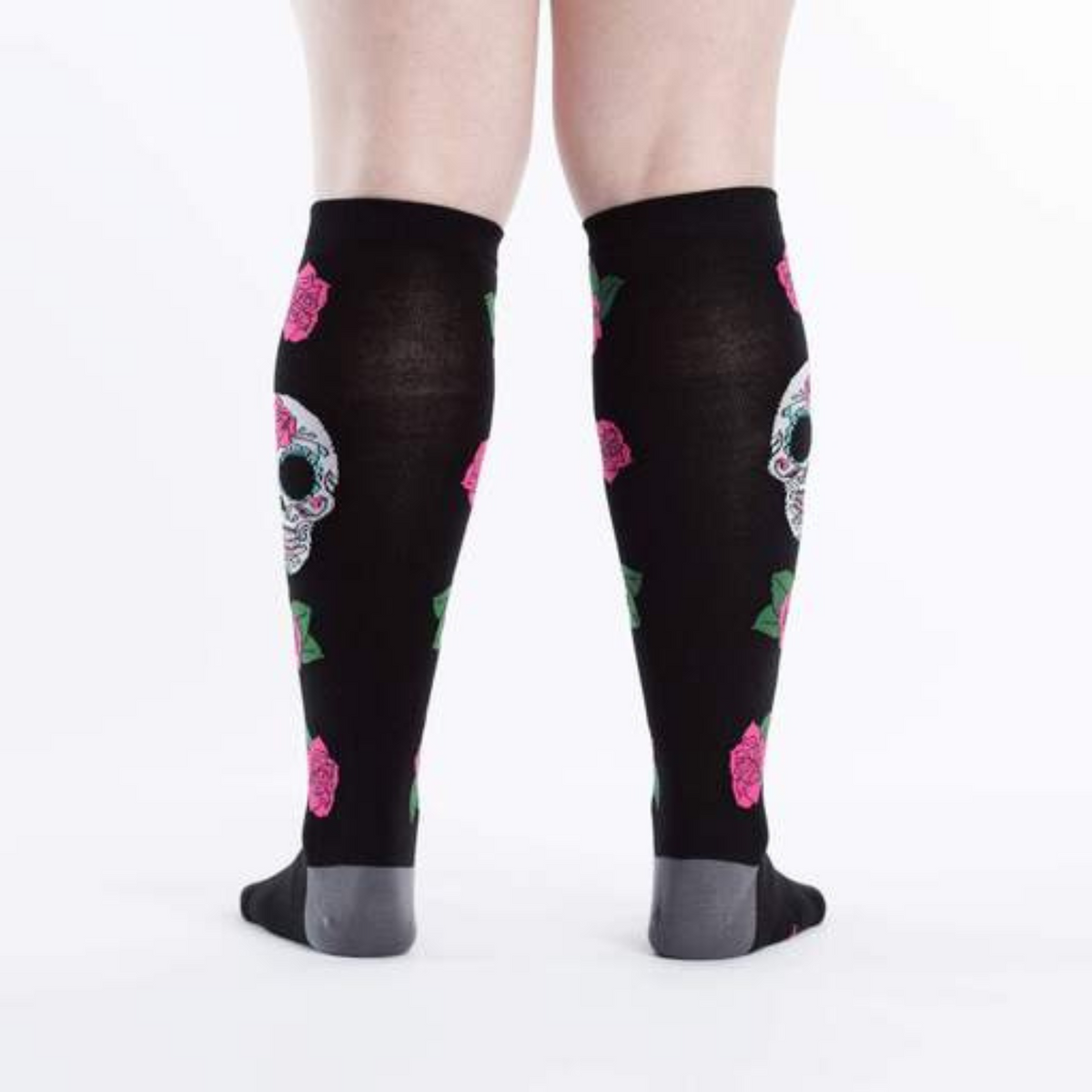 Sock It To Me Sugar Skull women&#39;s knee high sock featuring black sock with red roses all over and large Day of the Dead Sugar Skull. Socks worn by model seen from behind. 