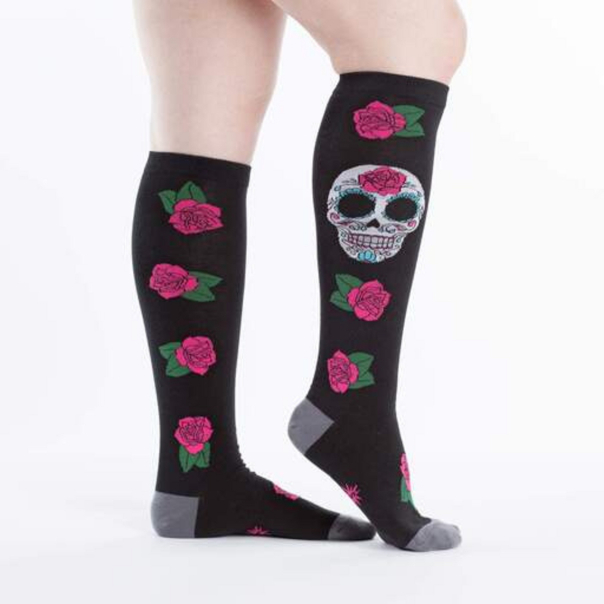 Sock It To Me Sugar Skull women&#39;s knee high sock featuring black sock with red roses all over and large Day of the Dead Sugar Skull. Socks worn by model seen from side. 