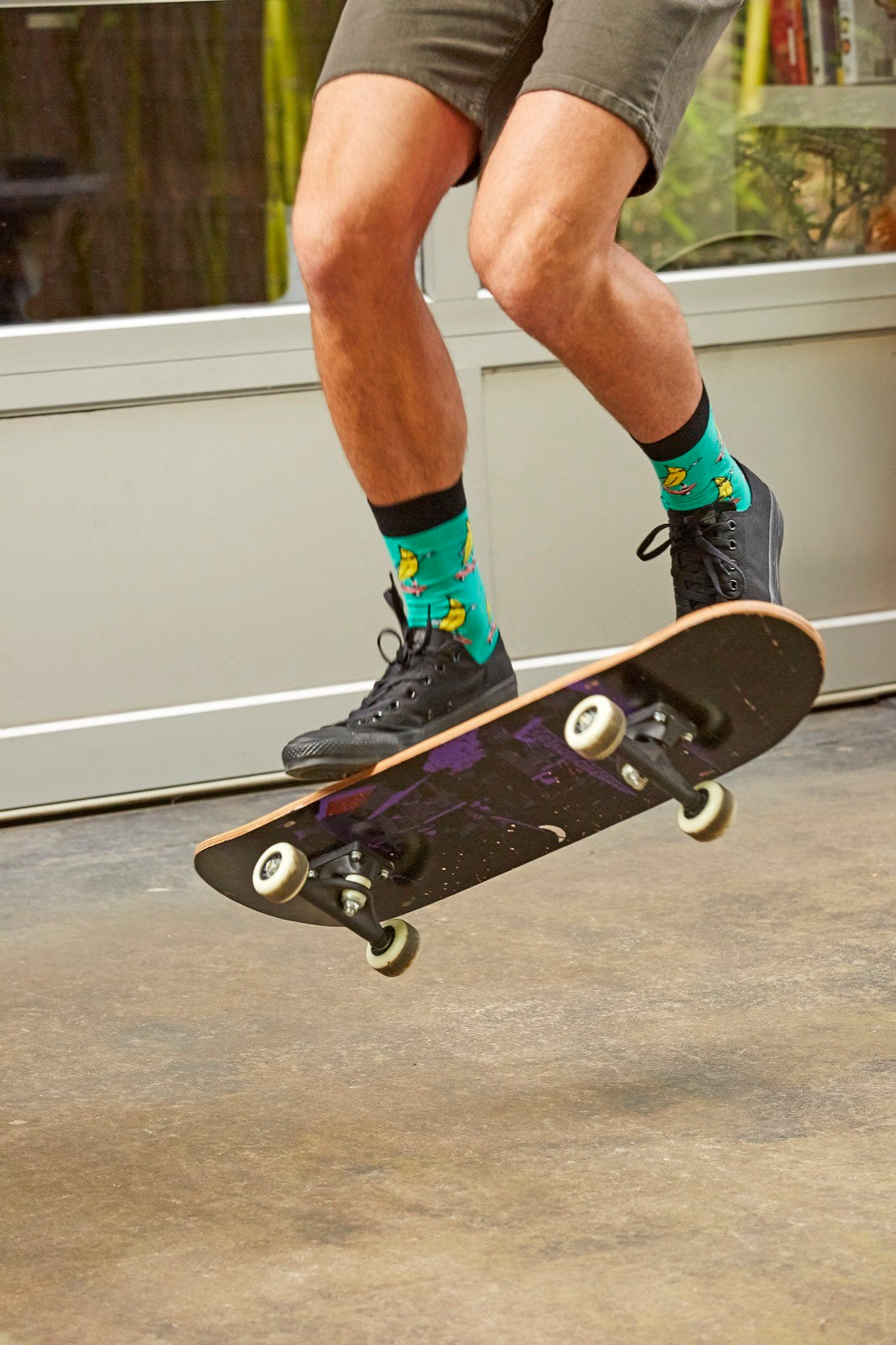 model wearing Sock It To Me Peeling Out men&#39;s crew sock featuring green sock with bananas in sunglasses on skateboards all over.