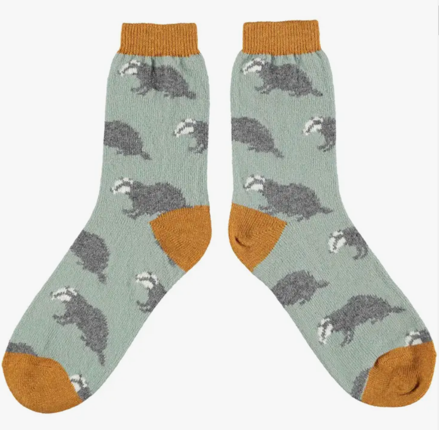 Catherine Tough Badger lambswool women&#39;s crew socks featuring ginger cuff, heel and toe with gray badgers on a soft green background