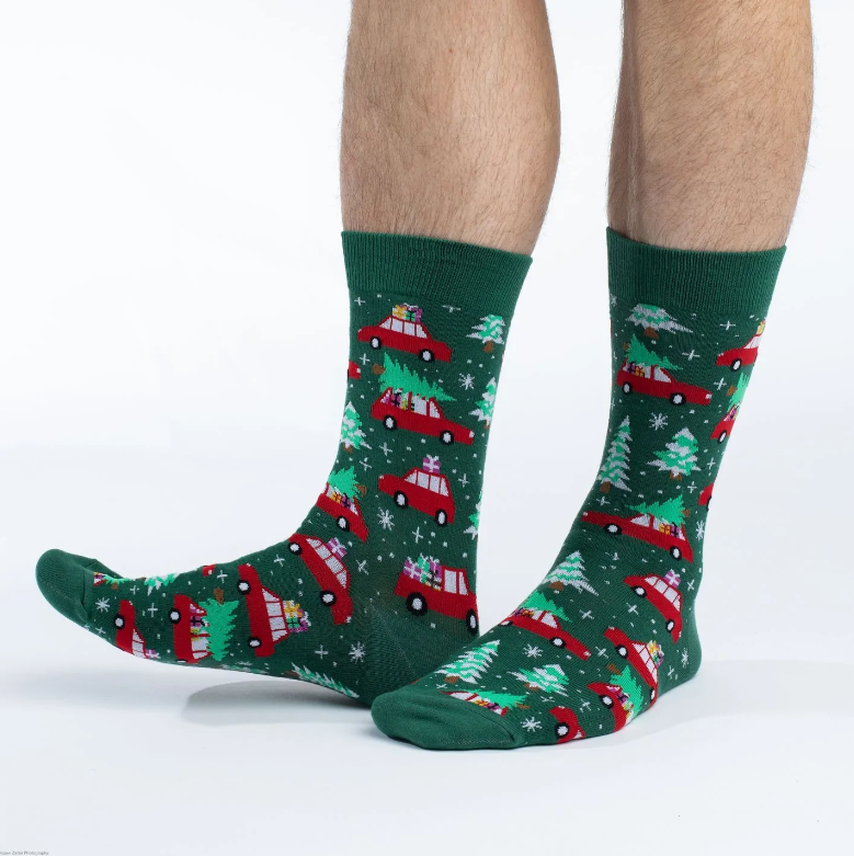 Good Luck Sock Christmas Tree men&#39;s crew sock featuring green sock with red cars with trees and presents. Socks worn by model seen from side. 