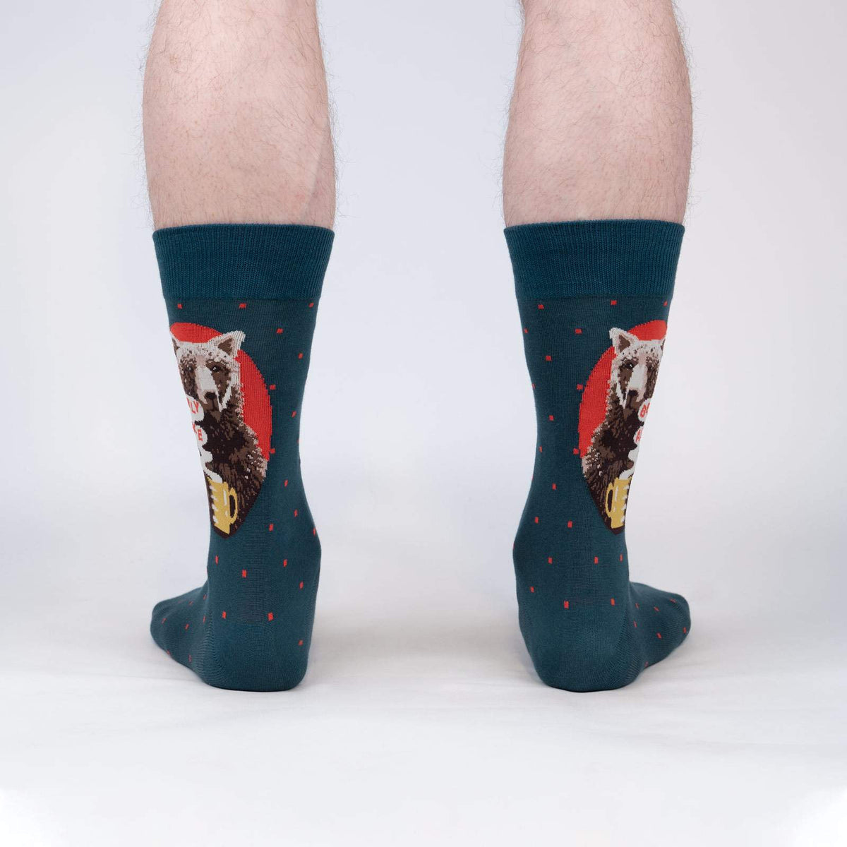 Sock It To Me Bearly Awake women&#39;s and men&#39;s crew sock featuring blue sock with small red polka dots and picture of bear holding a cup of coffee and the saying &quot;bearly awake&quot;. Socks worn by model seen from back.