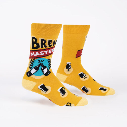Sock It To Me Brew Master men&#39;s crew sock. Featuring yellow sock with &quot;Brew Master&quot; and various beer glasses all over. Socks worn by display feet.  