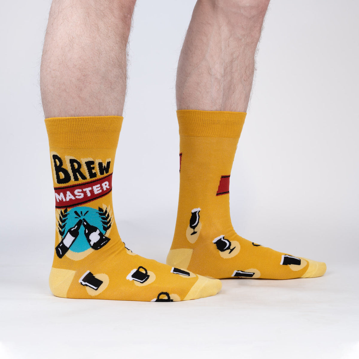 Sock It To Me Brew Master men&#39;s crew sock. Featuring yellow sock with &quot;Brew Master&quot; and various beer glasses all over. Socks worn by model seen from the side. 