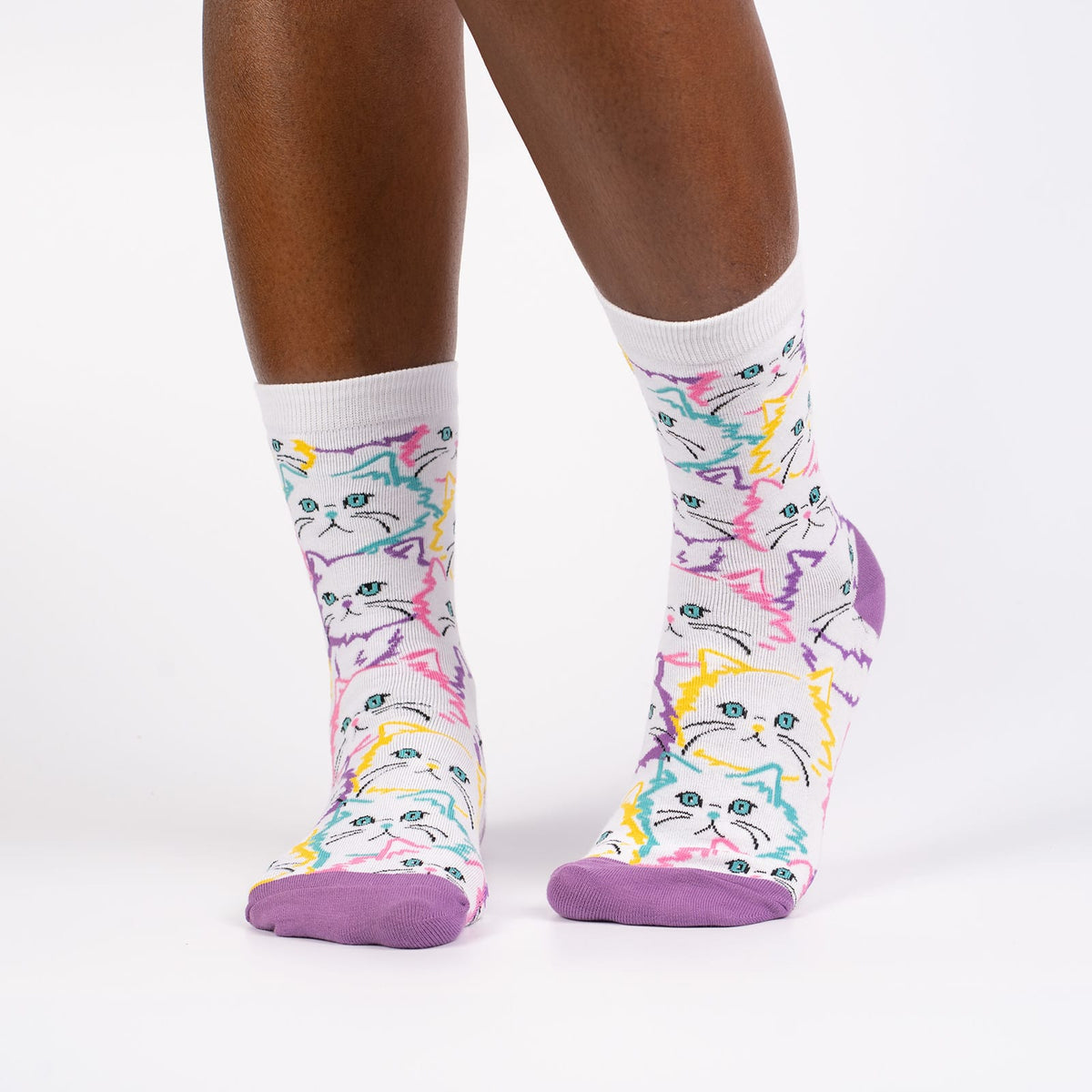 Sock It To Me Fur Real women&#39;s crew sock featuring white sock with lavender heel and toe with white cats outlined in pastel colors. Socks worn by model seen from front. 