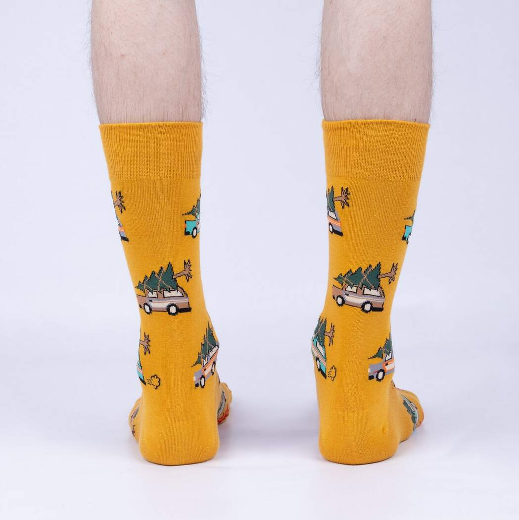 Sock It To Me Little Full, Lotta Sap men&#39;s crew sock featuring mustard yellow sock with images of station wagons with christmas trees tied to the top. Socks shown on model&#39;s feet from behind.. 