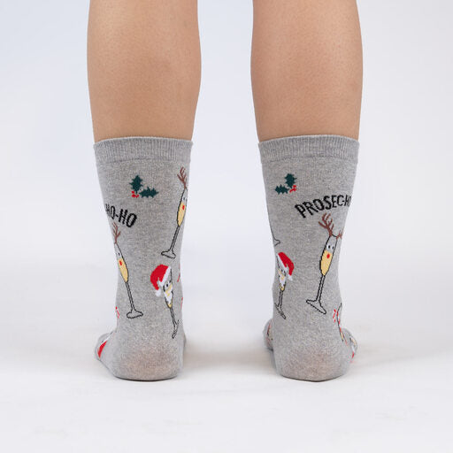 Sock It To Me Prosec-Ho-Ho-Ho women&#39;s crew sock featuring shimmery silver socks with glasses of Prosecco dressed in Christmas outfits and &quot;Prosec-Ho-Ho-Ho&quot;. Socks worn by model seen from behind.. 