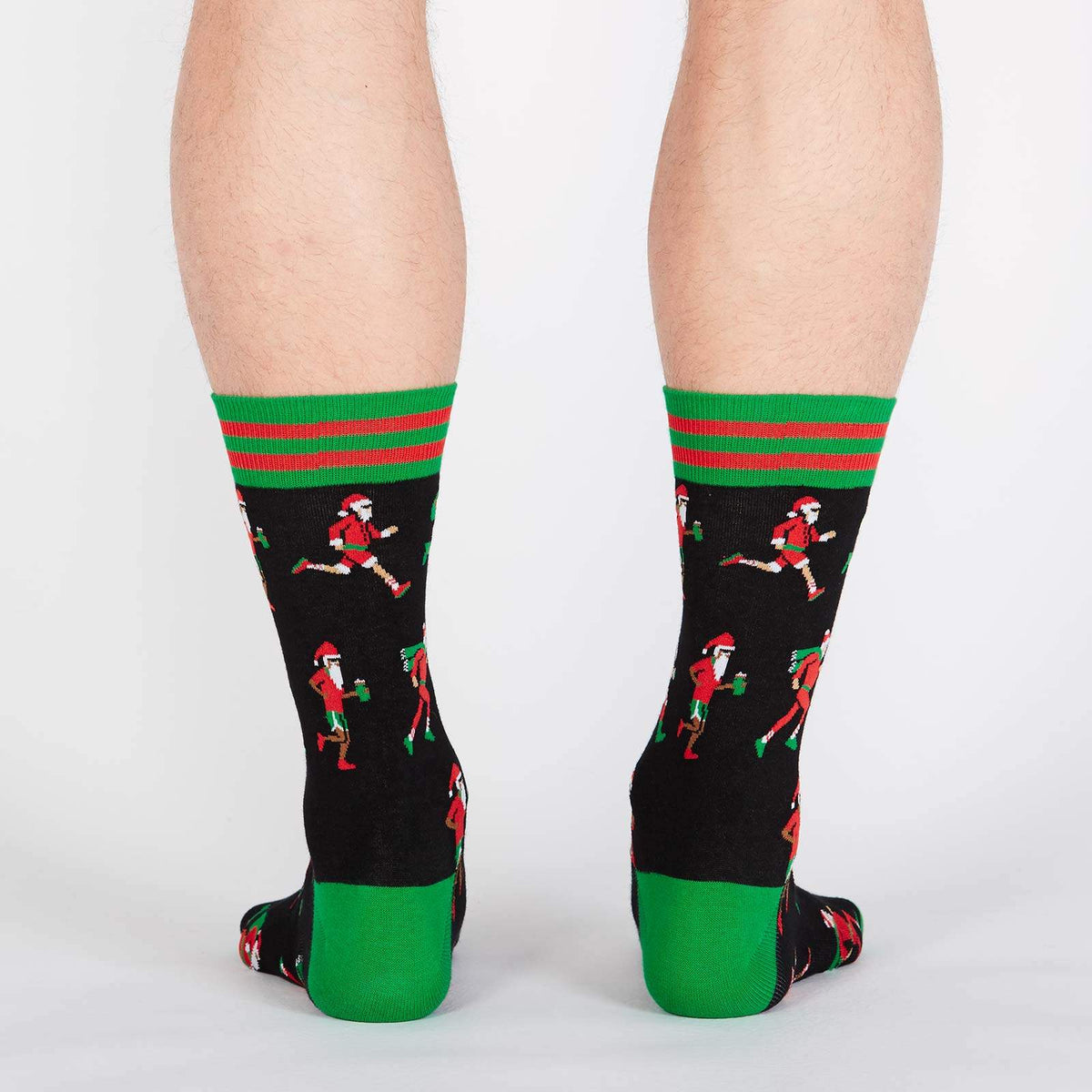 Sock It To Me Santa Run men&#39;s crew sock featuring black sock with various Santa Clauses running. Socks shown on model from behind. 