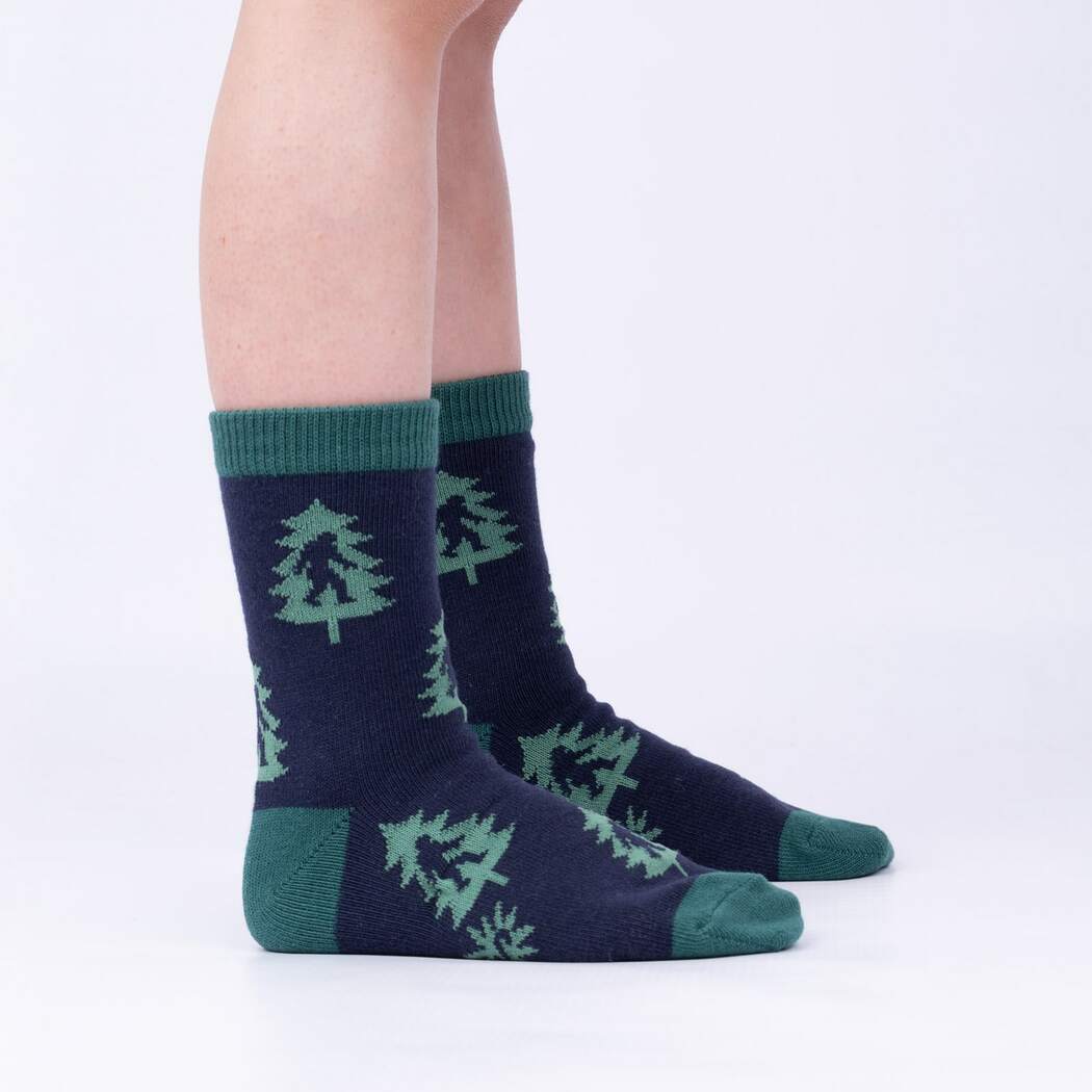 Sock It To Me Sasquatch Camp Out 3-pack kids&#39; crew socks featuring Sasquatch silhouette on a tree socks on model seen from side. 