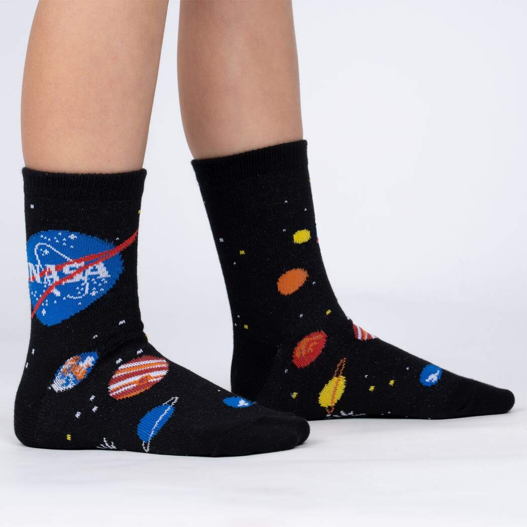 Sock It To Me Solar System (GLOWS IN THE DARK!) 3-pack kids&#39; socks featuring black socks with NASA logo and planets all over worn by model seen from the side