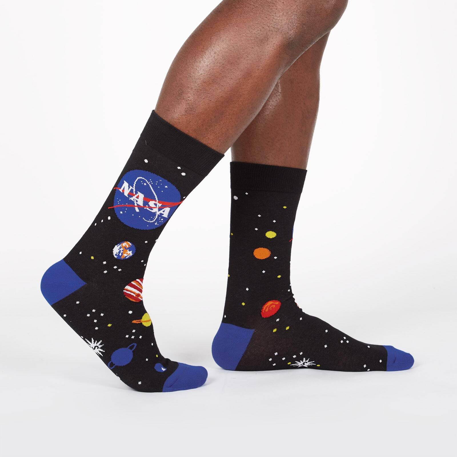 Sock It To Me NASA Solar System men's crew socks featuring black sock with NASA logo and planets all over. Socks worn by model seen from side. 