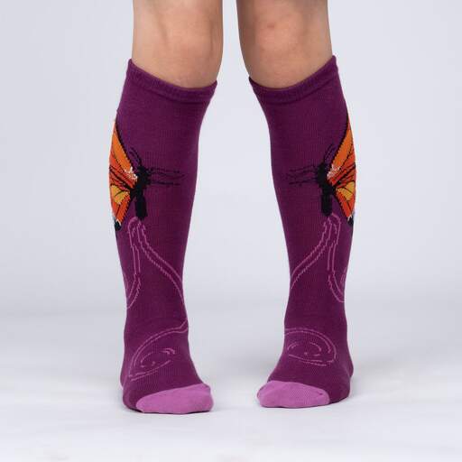 Sock It To Me The Monarch women&#39;s, kids&#39;, and extra-stretchy socks on model from side. Socks are purple featuring monarch butterfly. Shown on youth model from front.. 