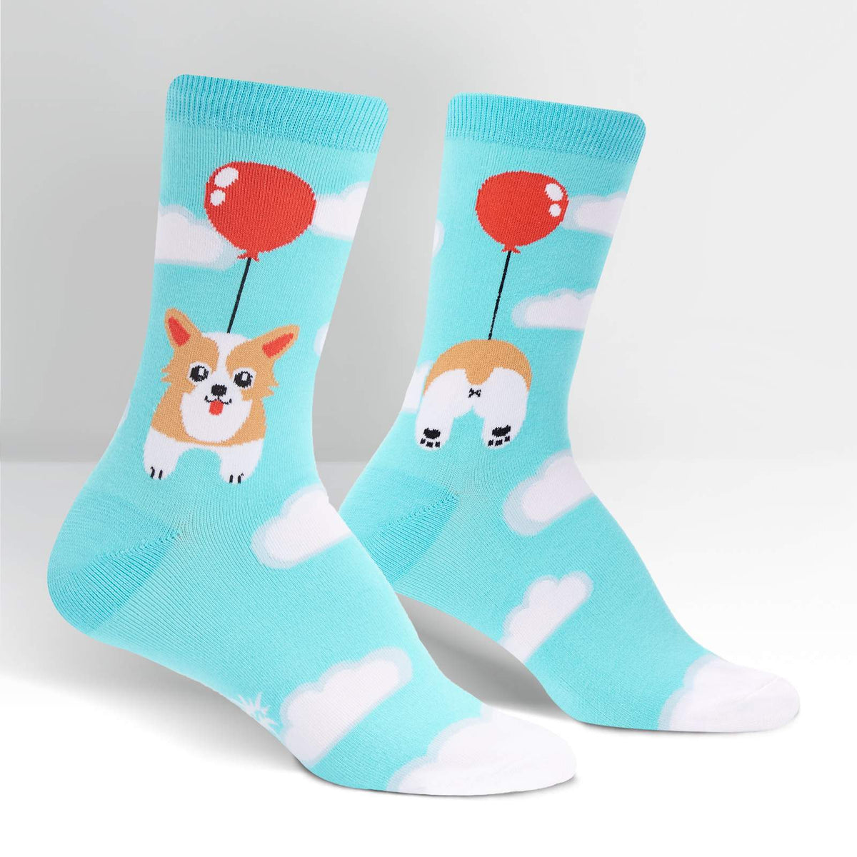 Sock It To Me Pup, Pup and Away women&#39;s crew socks featuring light blue socks with clouds all over and a Corgi dog floating by a red balloon, socks show front and back of Corgi dog. Socks shown on display feet seen from side. 