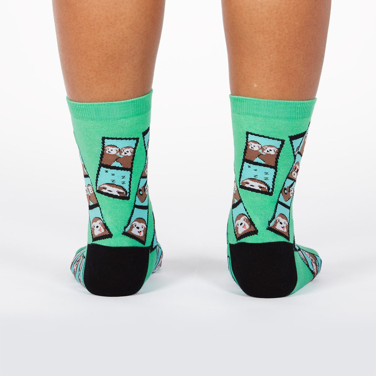Sock It To Me Oh Snap! women&#39;s crew sock. Featuring green sock with photo booth images of sloths all over. Socks worn by model seen from behind. 