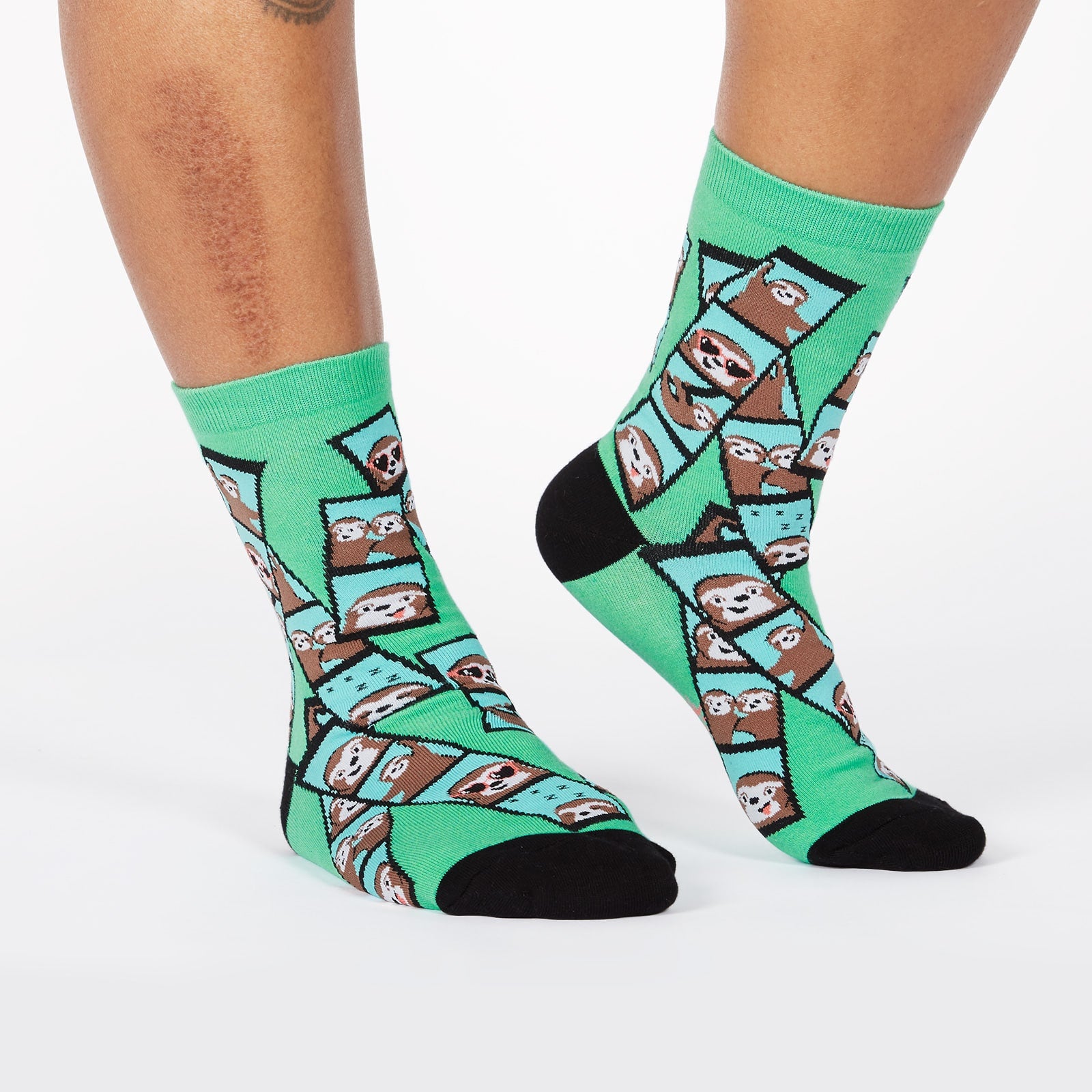 Sock It To Me Oh Snap! women's crew sock. Featuring green sock with photo booth images of sloths all over. Socks worn by model seen from front. 