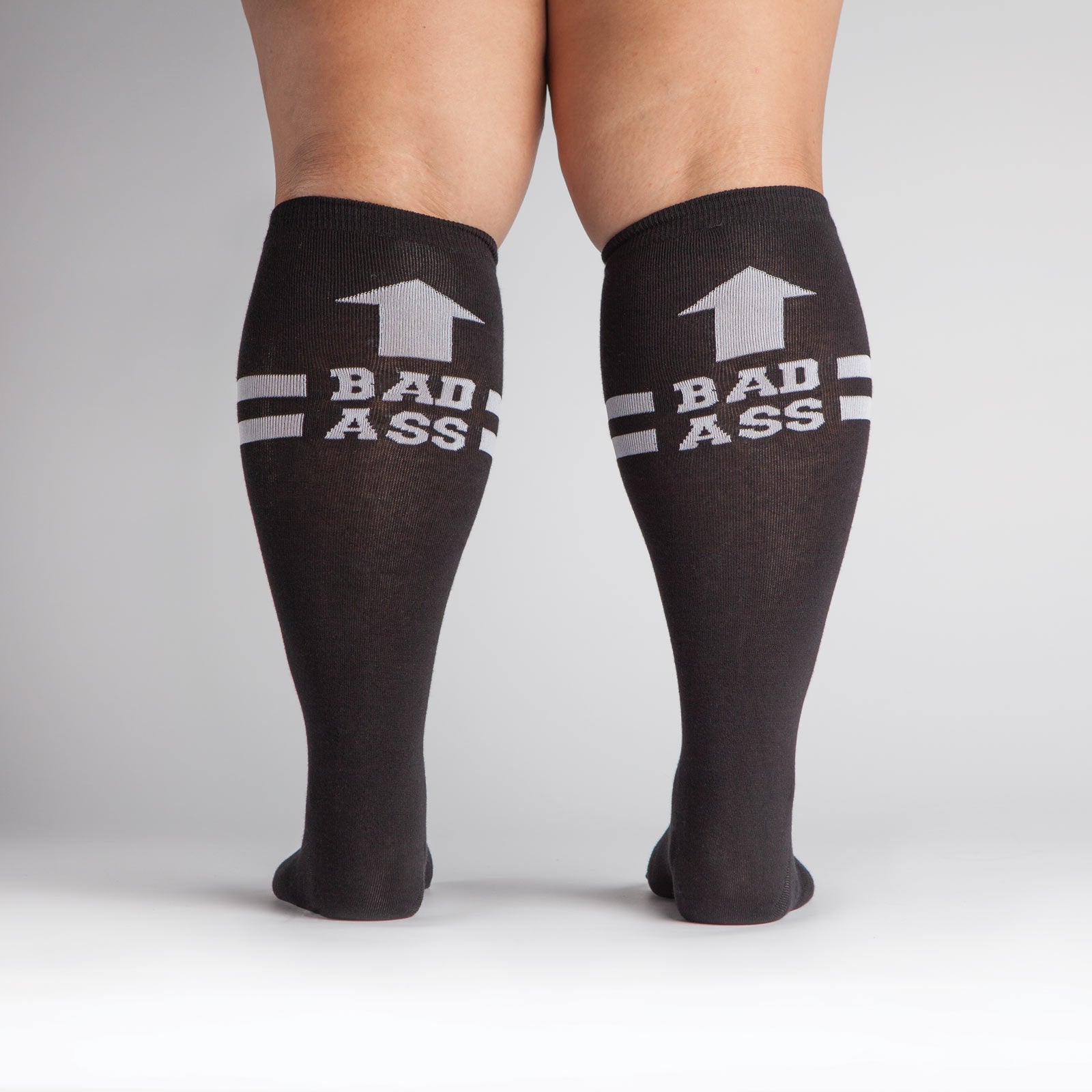Sock It To Me Bad Ass extra-stretchy women's and men's socks featuring black socks with "Bad Ass" and arrow pointing up worn by model shown from back