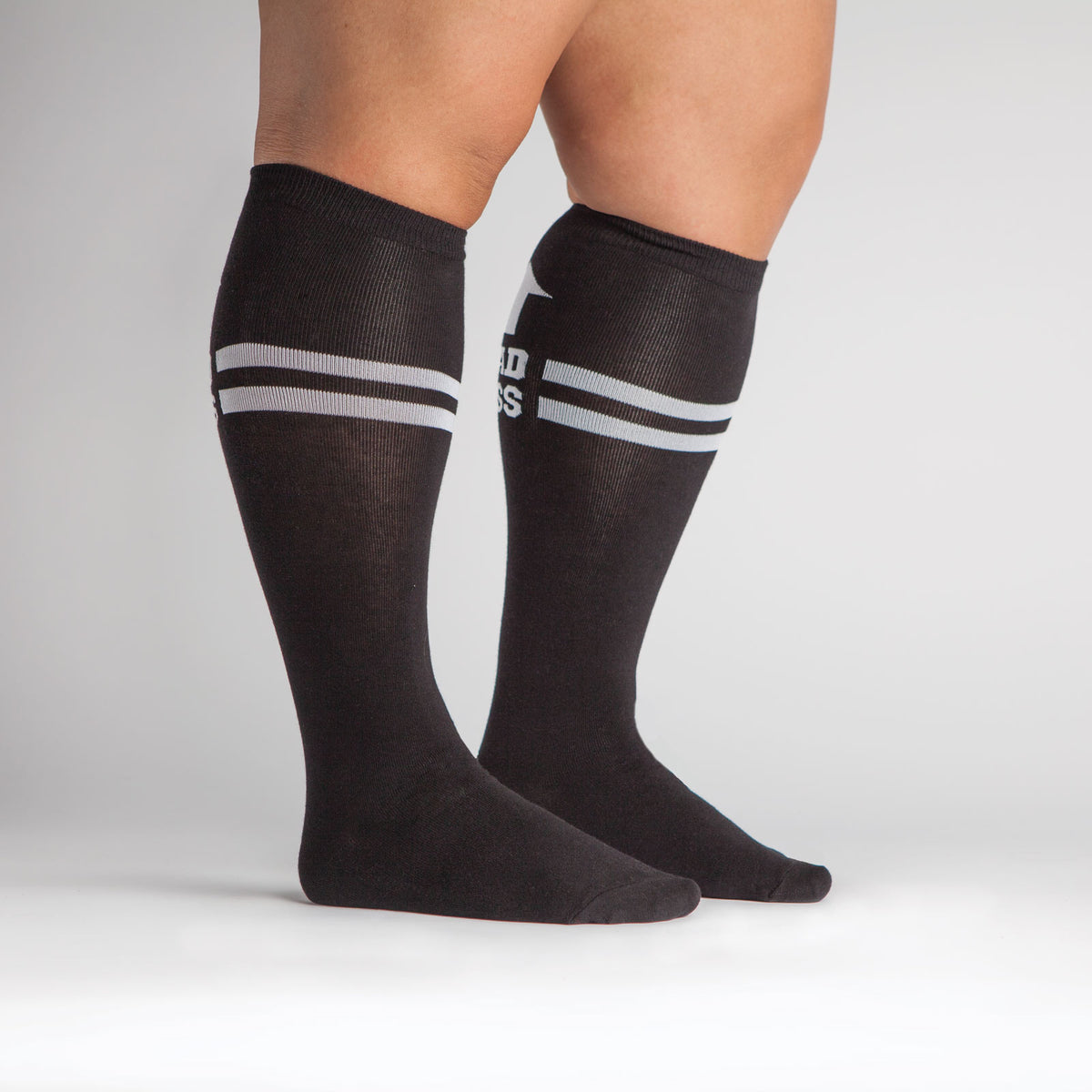 Sock It To Me Bad Ass extra-stretchy women&#39;s and men&#39;s socks featuring black socks with &quot;Bad Ass&quot; and arrow pointing up worn by model shown from side