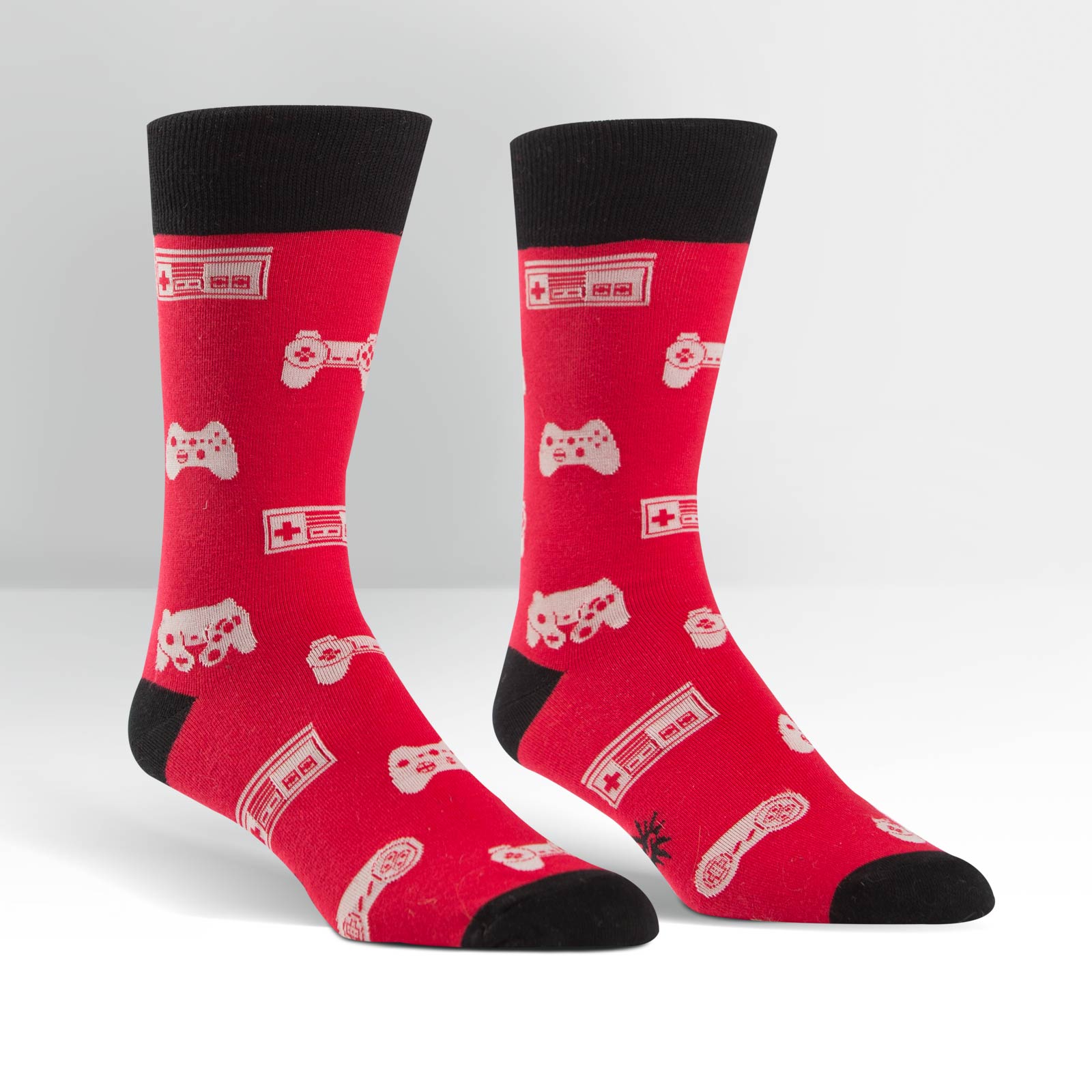 Sock It To Me Multi-Player men's crew sock featuring red sock with black cuff, heel, and toes and white video game controllers all over. Socks shown on display feet. 