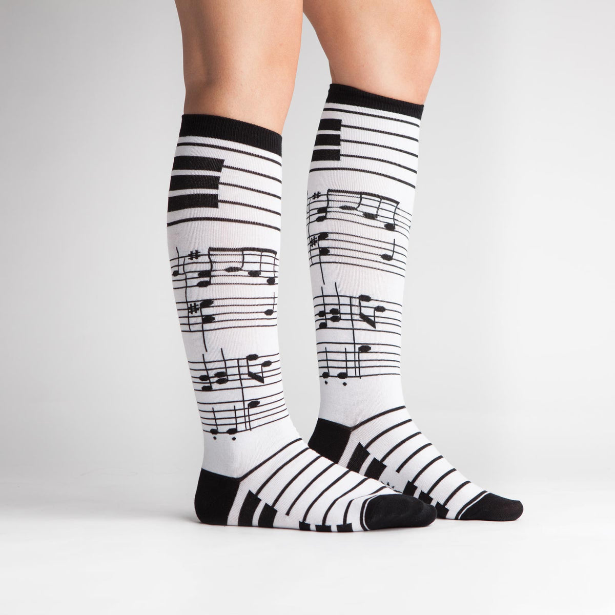 Sock it to Me Foot Notes women&#39;s knee high sock featuring white sock with black musical notes all over on model from side